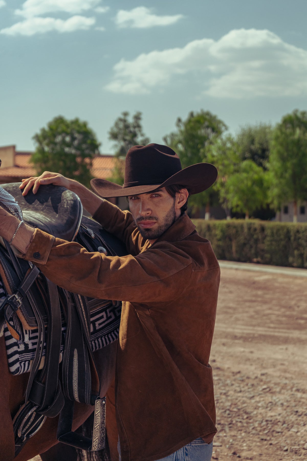 Modelo con texana John café junto a la montura de un caballo